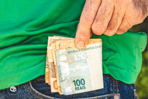 Mão colocando cédulas de 100 reais em bolso, recebimento de herança precatório